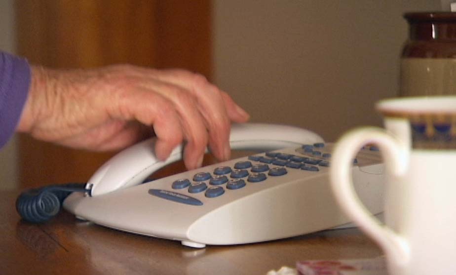 The hand of an elderly woman reaches to answer a landline phone.