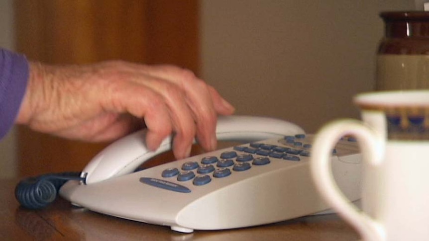 The hand of an elderly woman reaches to answer a landline phone.