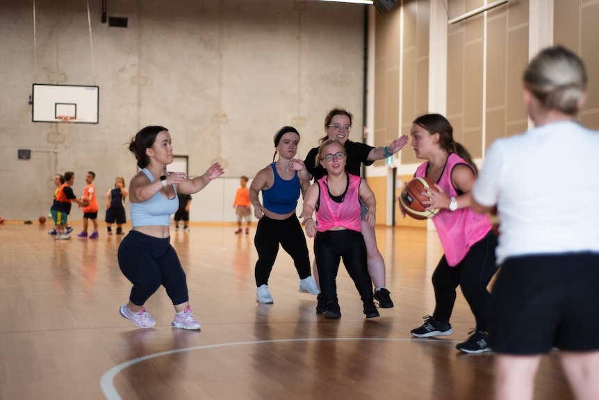 A group of female short statured basketballers are on the court training. 