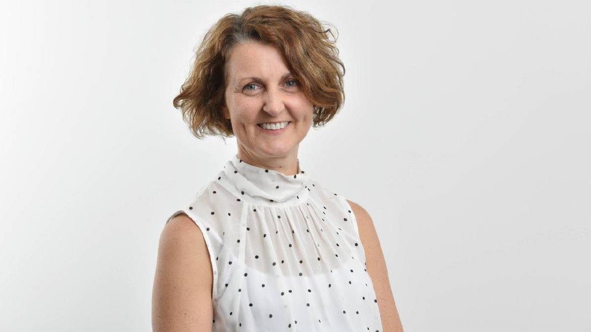 A woman in a white shirt smiling at the canera in a white room.