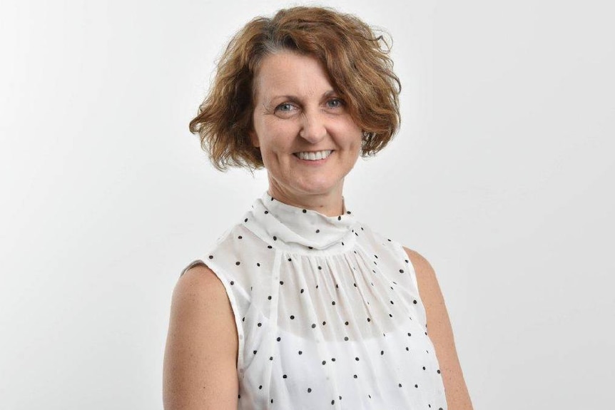 A woman in a white shirt smiling at the canera in a white room.