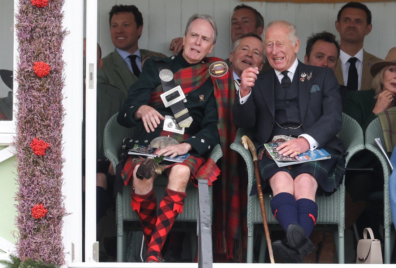 A man in a kilt, sitting and laughing, while several other people look on.