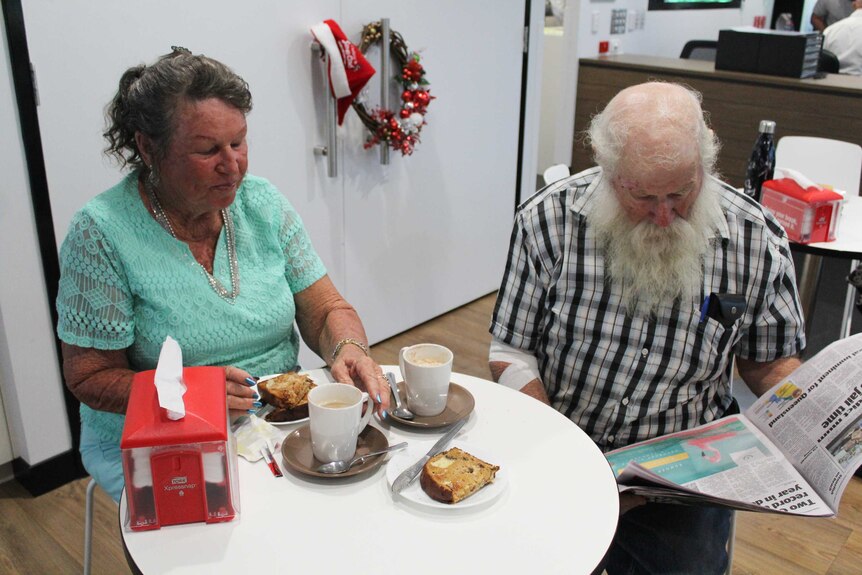 two people sit around a small round table eating raisin toast and coffee while reading the paper
