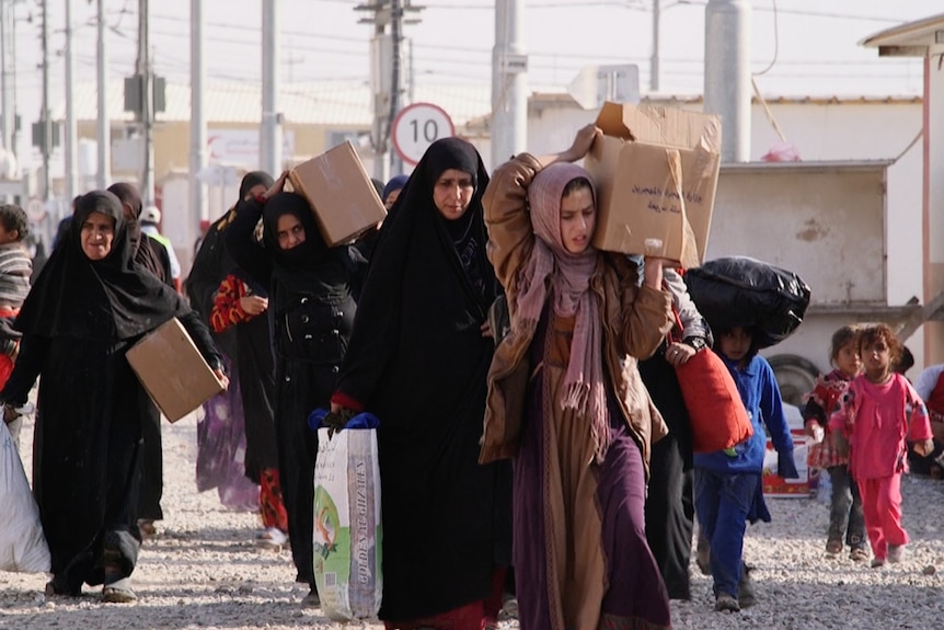 Women wearing hijabs carrying boxes and supplies in Iraq.