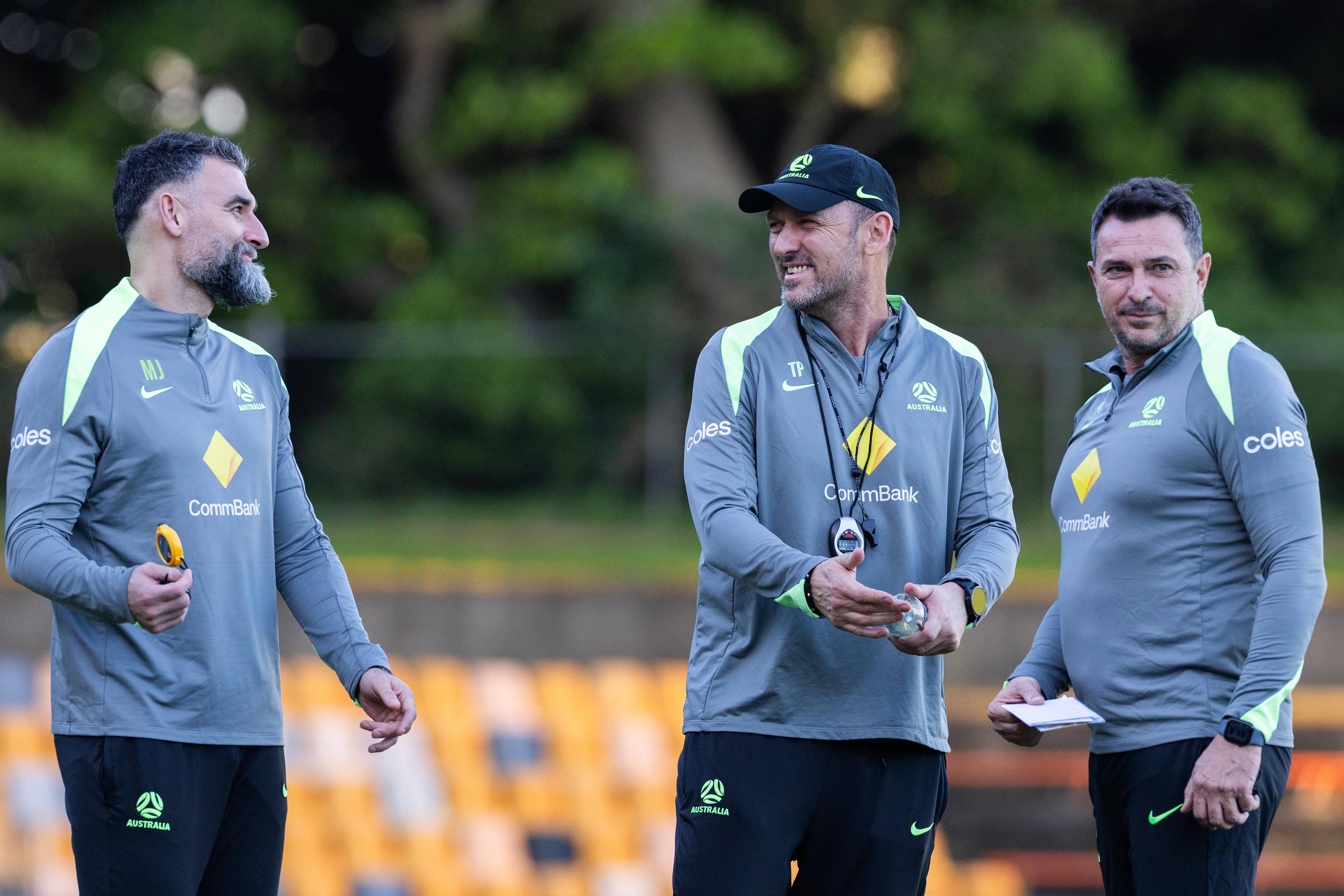 Os membros da equipe técnica do Socceroos, Mile Jedinak, Tony Popovic e Paul Okon, sorriem durante uma sessão de treinamento.