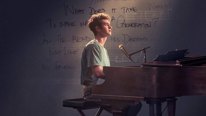 Andrew Garfield sitting at a piano with  a microphone on stage in the movie Tick, Tick...Boom!