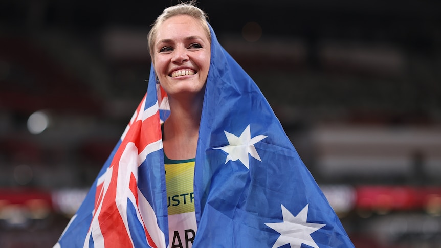 An Australian female javelin thrower smiles as she wears her national flag over her shoulders.