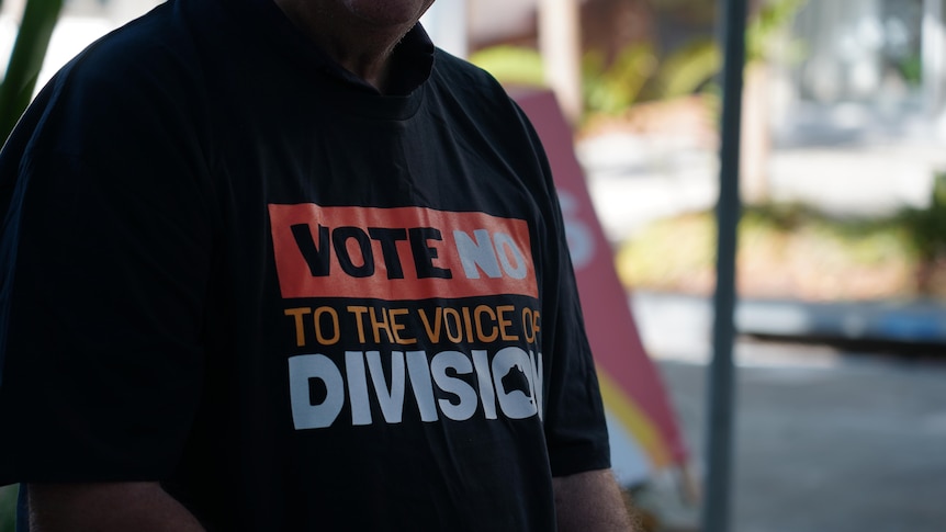 A person wearing a dark t-shirt with the words 'vote no to the voice of division'. 