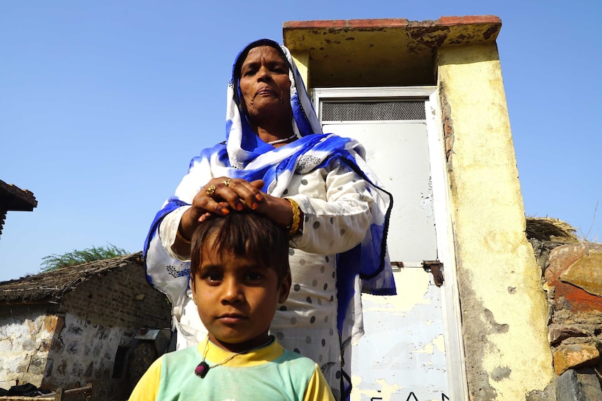 A woman and a child stand in front of an outdoor toilet. 