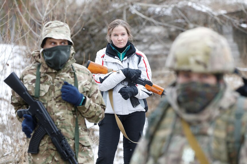 A young woman holds a assault rifle in her arms during a training exercise in snow.