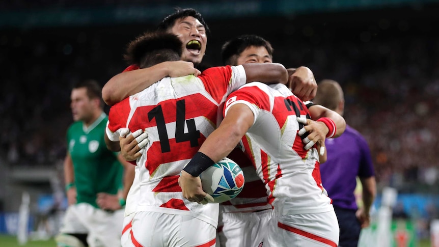 Japan players in red and white striped shirts hug and jump together