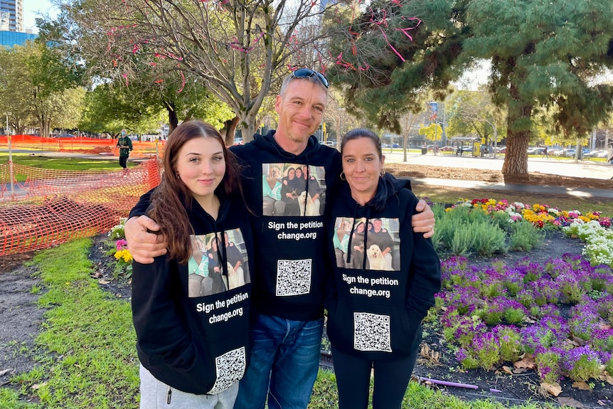 A man and two women in a park wearing identical black hoodies with a petition QR code and photo on it