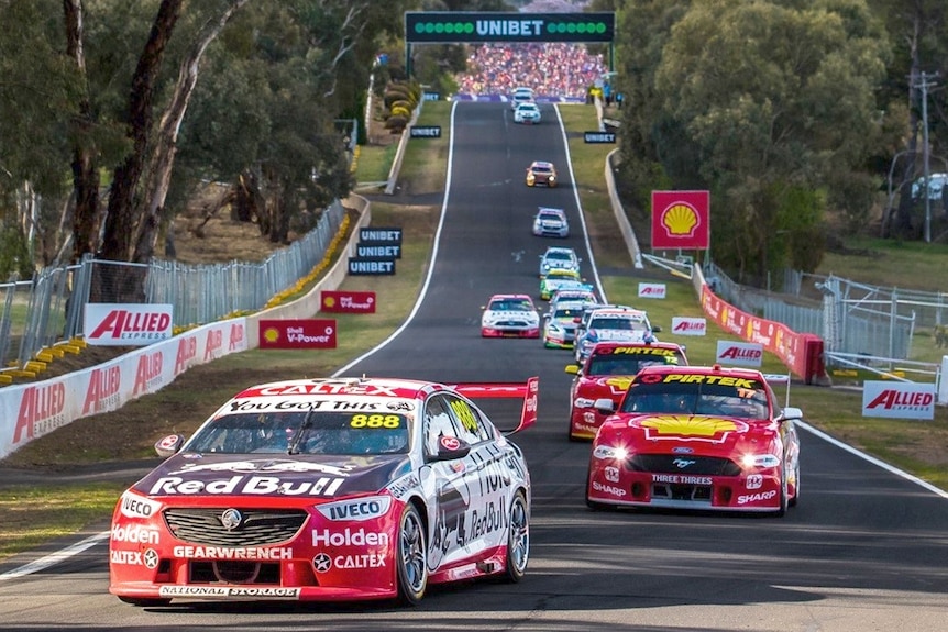 Long view of supercars coming up mountain straight led by car 888 with car 17 second and a long line of other cars .