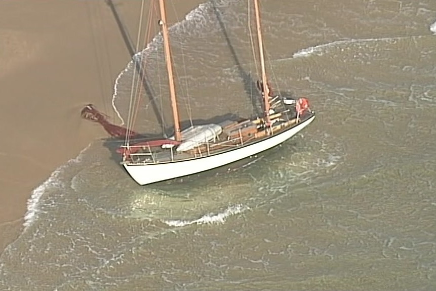 A yacht wallows in shallow water on a beach.