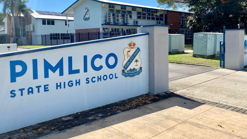 A picture of a school sign with school buildings in the background.