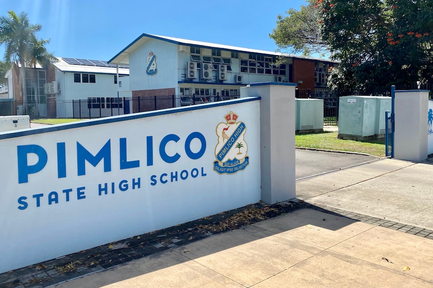 A picture of a school sign with school buildings in the background.