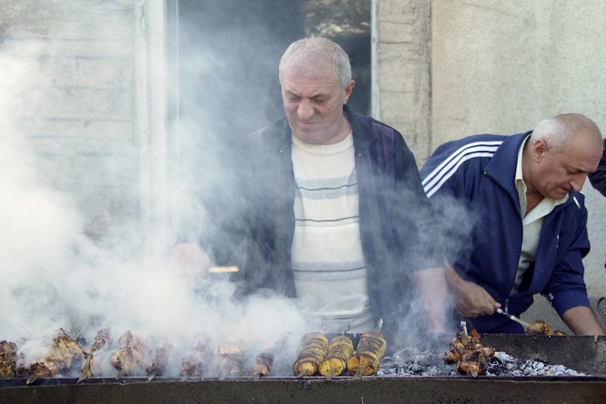 A man cooks meat over a smoky barbecue.