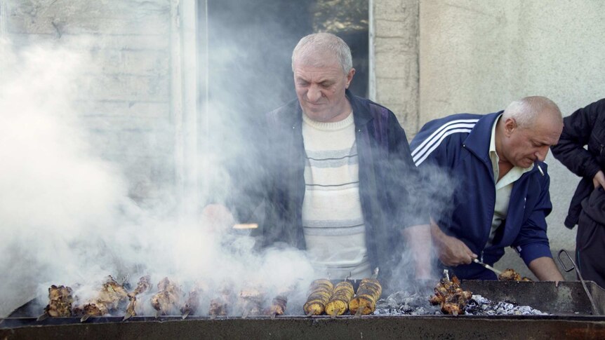 A man cooks meat over a smoky barbecue.