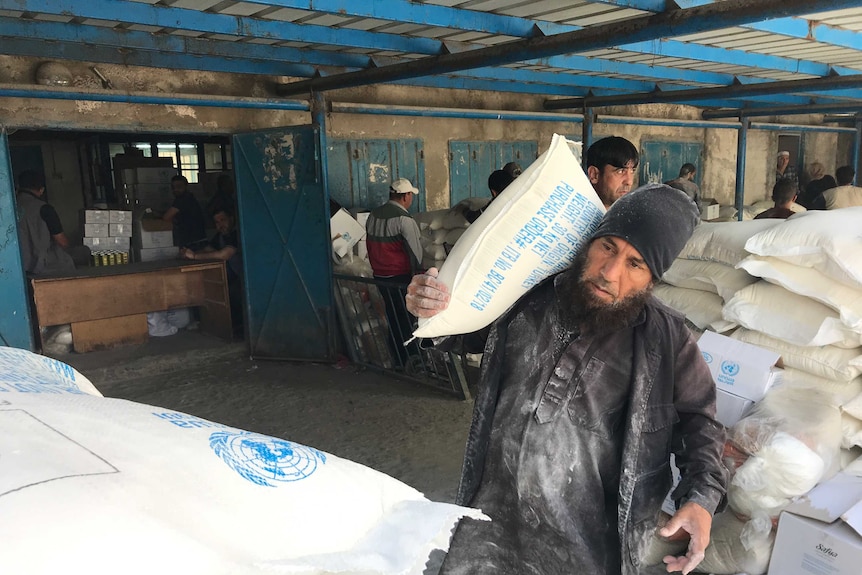 A man carries a sack of rice in a warehouse