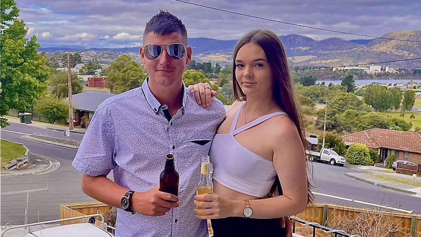 A man and a woman, both holding drinks, smile at the camera.