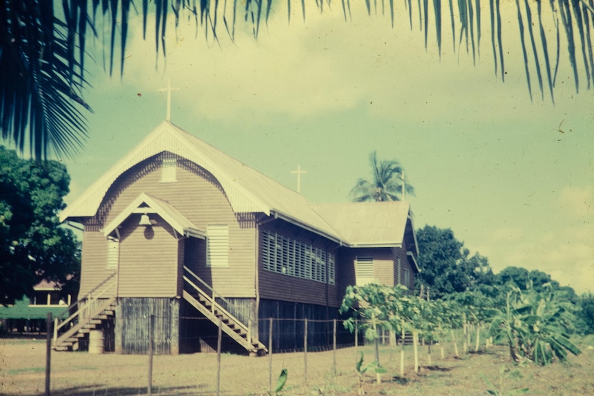 An elevated wooden church surrounded by palm trees 