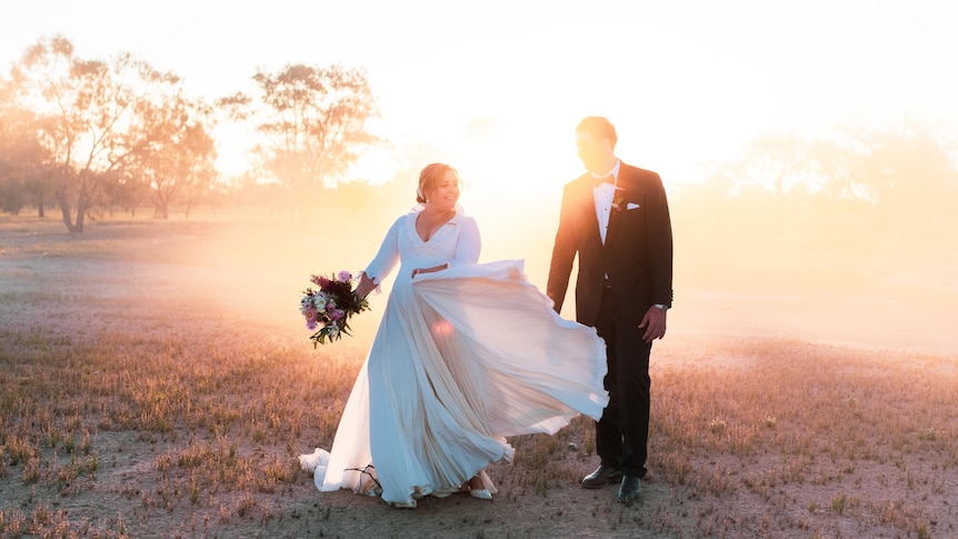 A bride and groom smile at each other in dusty setting