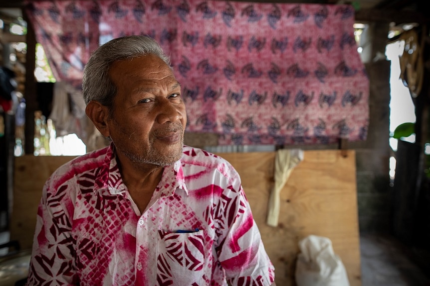 Community leader Teakamatang sits in a shack wearing a Hawaiian shirt.