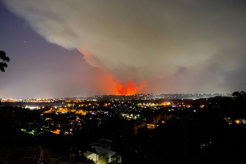 large fire at night billows over residential area with lots of lights on