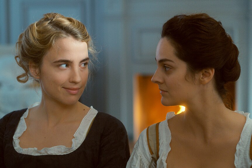 Colour close-up still of Adèle Haenel and Noémie Merlant looking at each other in 2019 film Portrait of a Lady on Fire.