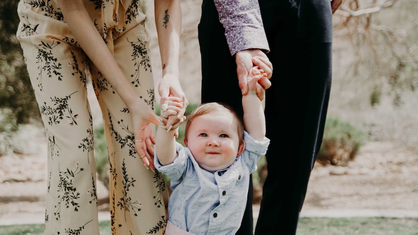 a man and woman are holding the hands of a happy toddler that is obviously learning to walk