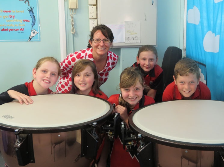 Five primary school students with their teacher sit behind the timpani (a type of drum)