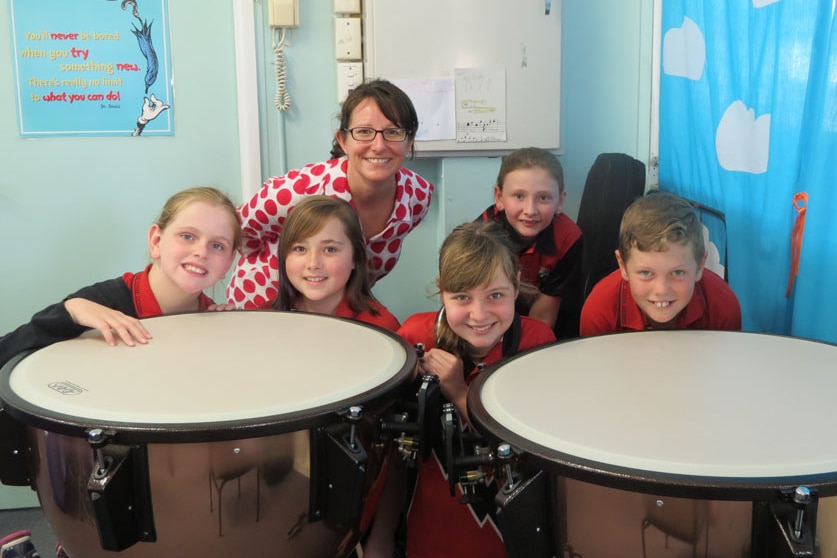 Five primary school students with their teacher sit behind the timpani (a type of drum)