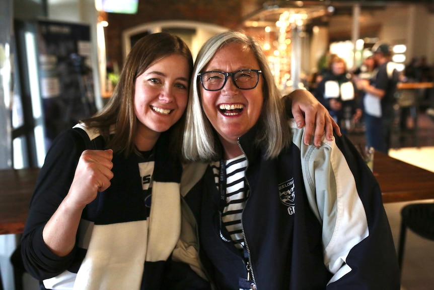 Two women dressed in Geelong merchandise, smiling and looking at the camera.