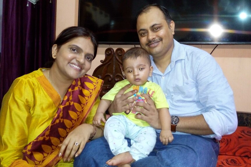 A woman dressed in a yellow sari sits next to a man with a child on his lap.