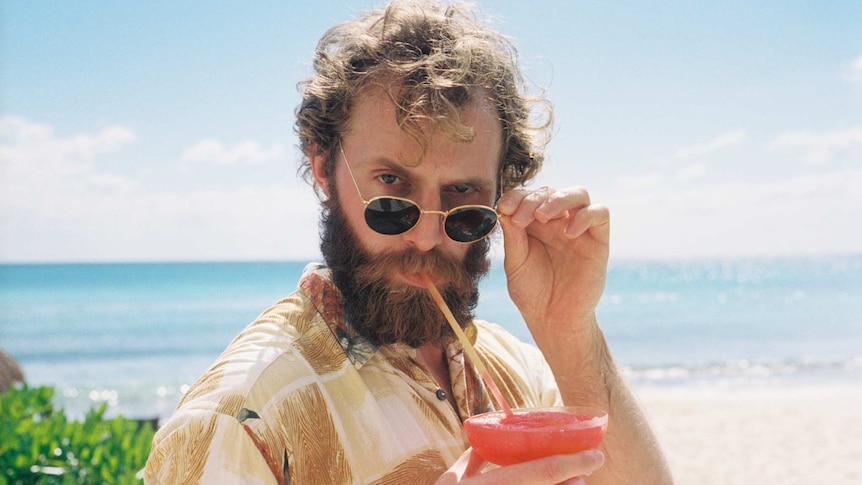 A man drinks a cocktail while standing on the beach