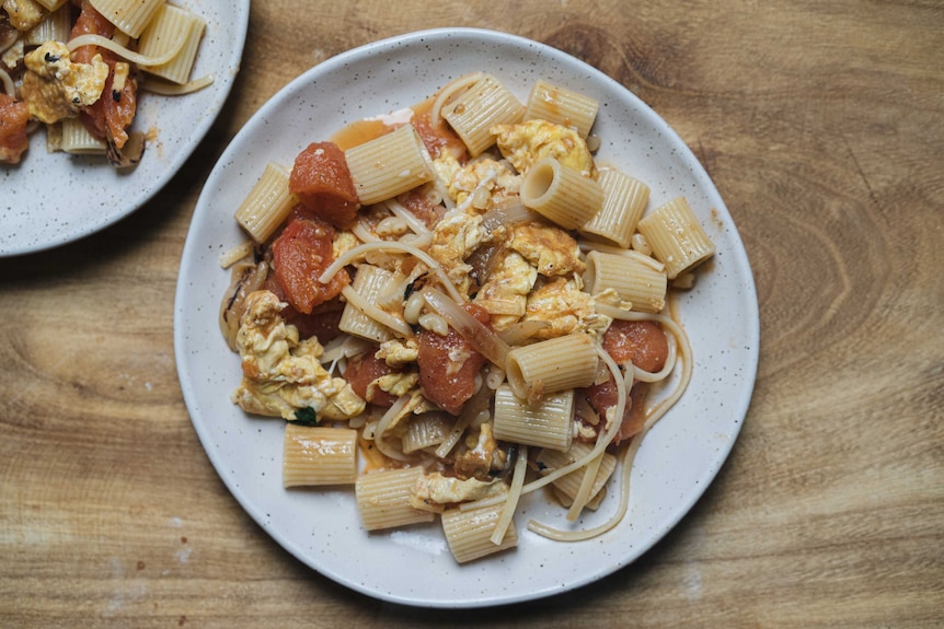 A bowl of pasta, pan fried tomatoes and egg make a simple meal during social distancing and coronavirus.
