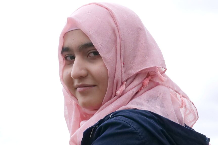 A close ups shot of a teenage girl wearing a pink hijab looking towards the camera. 