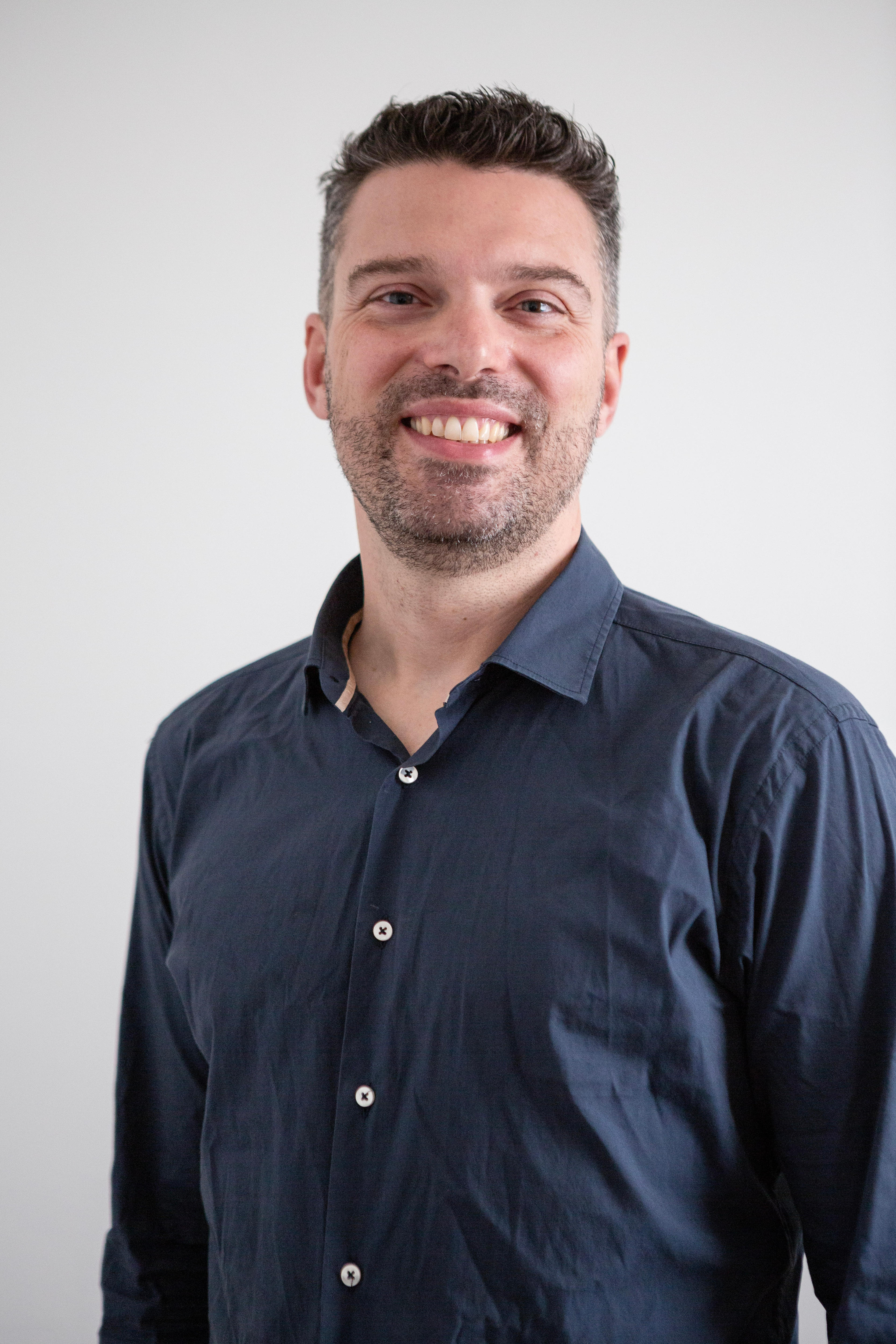 A headshot of a man in a navy blue shirt