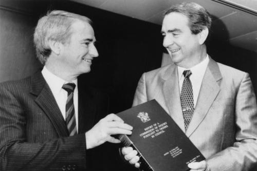 A black and white photo of the two smiling men standing side by side, each touching the bound report.