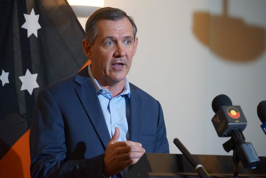 Michael Gunner speaks in to a microphone in front of an NT flag