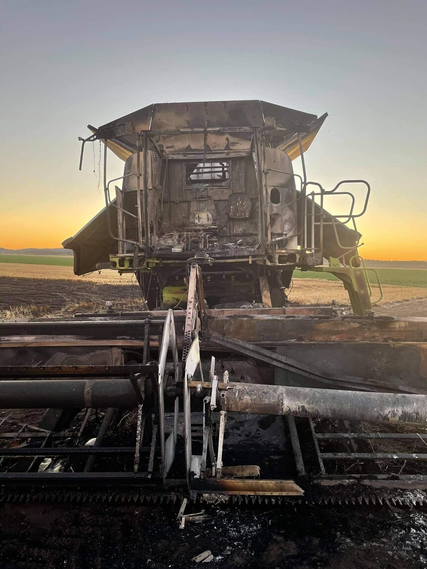 A burnt out header stands in a paddock with the sun setting in the distance