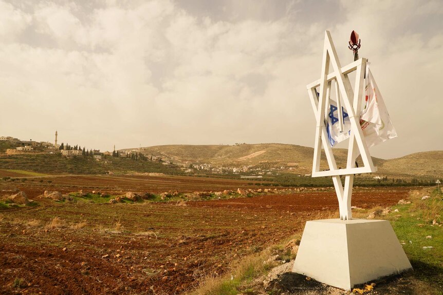 A white star of David statue sits on open land with a city in the background.