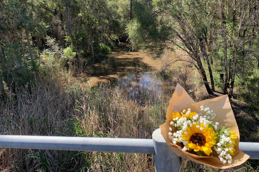 Flowers tied to the side of an overpass over a creek.