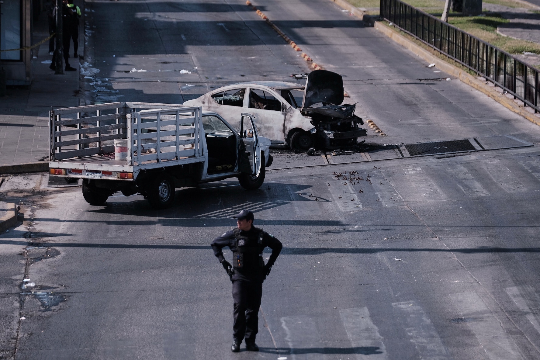 A police officer stands in front of two burned cars.