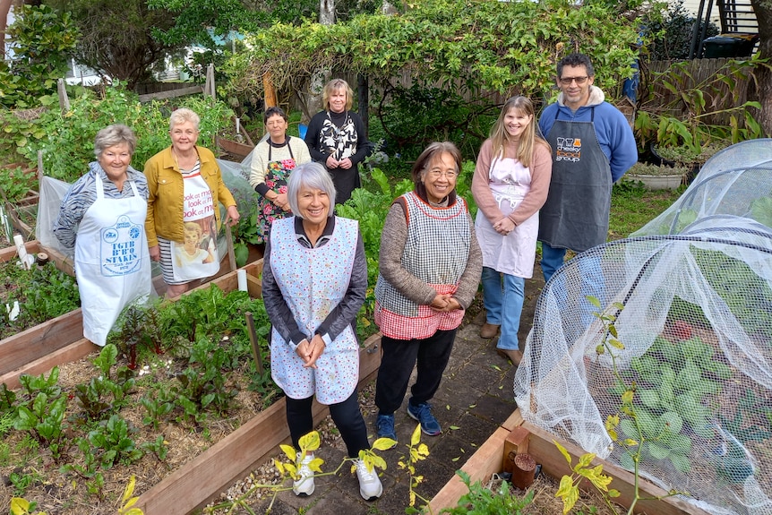 A group of about eight people standing in between rows of a vegetable garden, smiling.