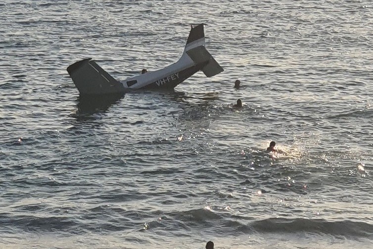 Beach goers watch as a plane sinks into the ocean