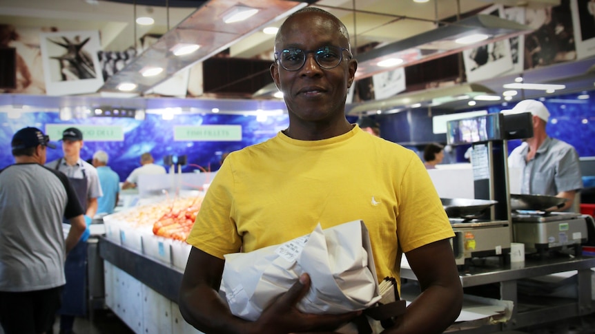 Mr Karagania is holding a packet of fish, standing in a fish market.