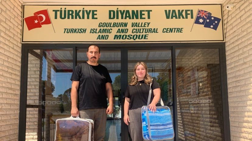 a man and a women stand outside the community centre holding donated blankets 