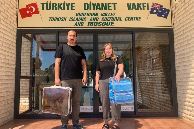 a man and a women stand outside the community centre holding donated blankets 