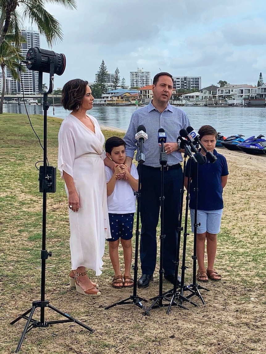Steve Ciobo  with his wife and two children with microphones and lights in front of them and water, boats and buildings behind